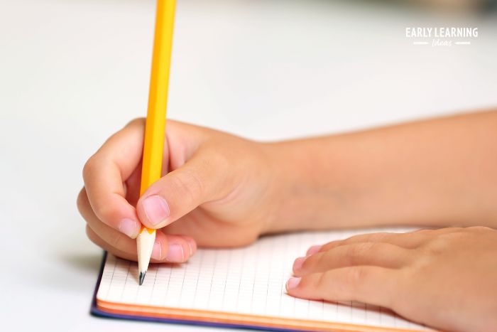 Child using the Dynamic tripod grip to write in a notebook with a black pencil. 